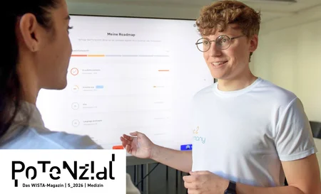 Zwei Personen im Gespräch vor einem Bildschirm mit einer Roadmap, eine Person trägt ein weißes T-Shirt und Brille
